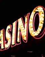 Brightly illuminated letters spell out 'CASINO' with glowing yellow bulbs and red outlines against a dark background.