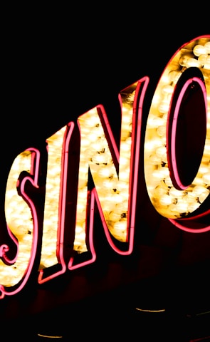 Brightly illuminated letters spell out 'CASINO' with glowing yellow bulbs and red outlines against a dark background.
