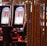 A pair of casino slot machines, each with detailed screens displaying various game outcomes and jackpot amounts. The chairs in front of the slot machines are dark and cushioned for comfort. The background features a hanging curtain made of golden ropes and other casino decorations are visible.