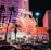 A brightly lit casino with neon lights in vibrant red, pink, and blue, featuring a large flamingo signage. Palm trees are visible in the foreground with vehicles passing by on the street at night.